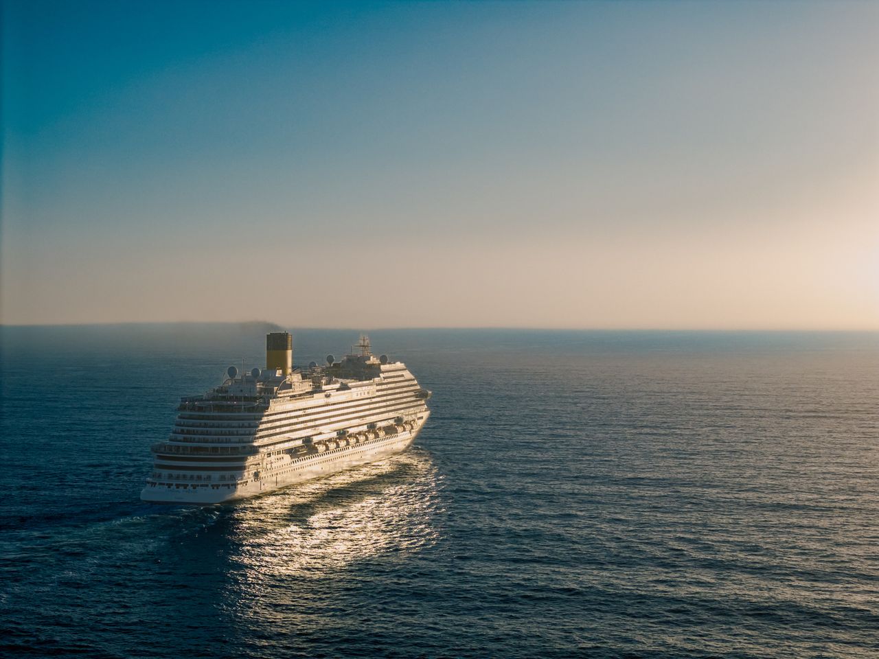 services-01 A cruise ship gracefully sails across the ocean at sunset, creating a tranquil scene.